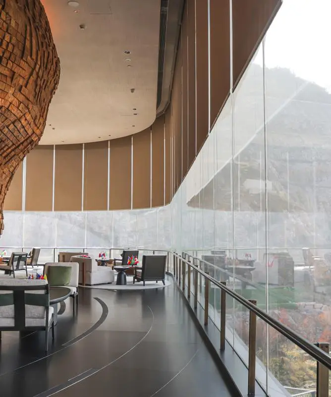 Curved wall of floor-to-ceiling glass with roller shades lowered